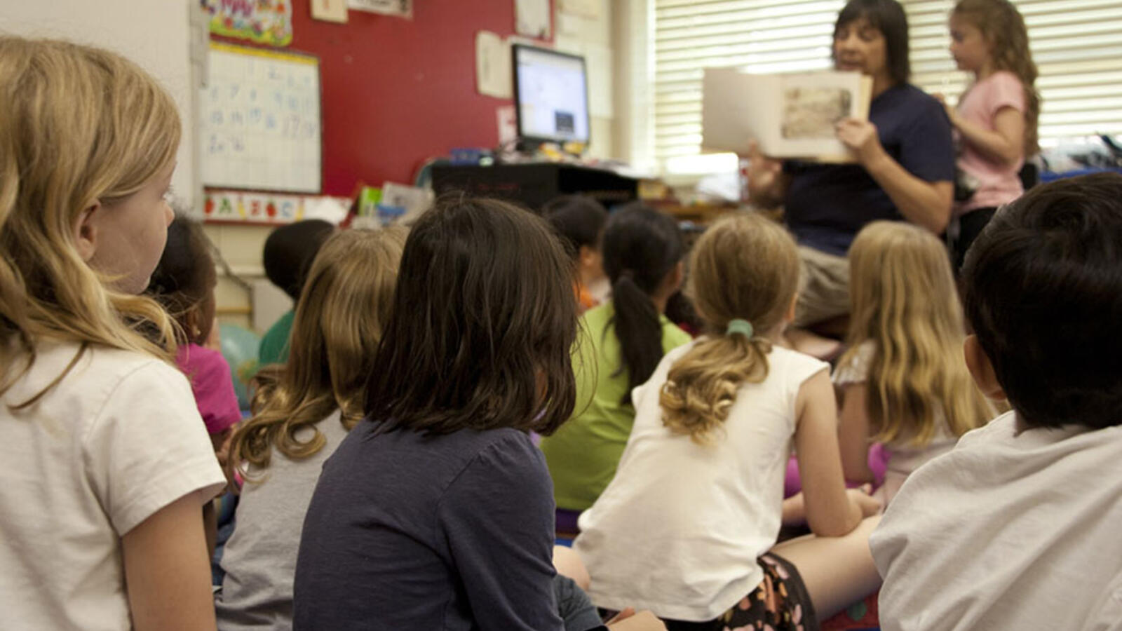 young students sitting on the floor in class listening to a woman read