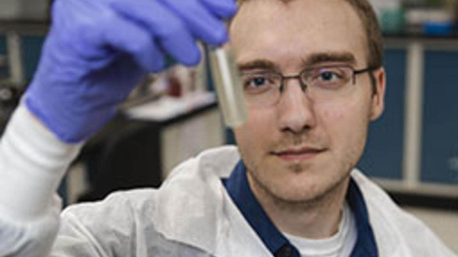 man in lab coat looking at vile