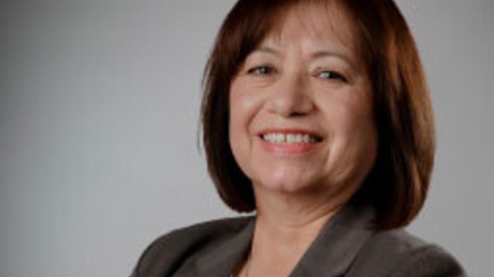 Debra Flores, Ph.D., standing for headshot with a studio backdrop