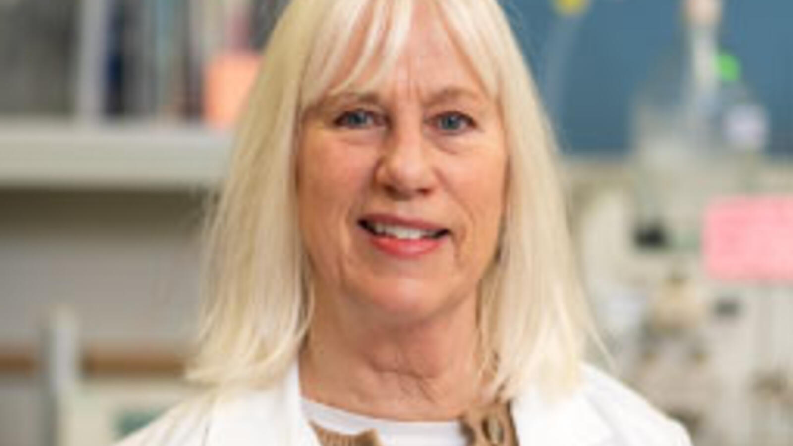 Woman researcher stands in her lab while wearing a white coat.