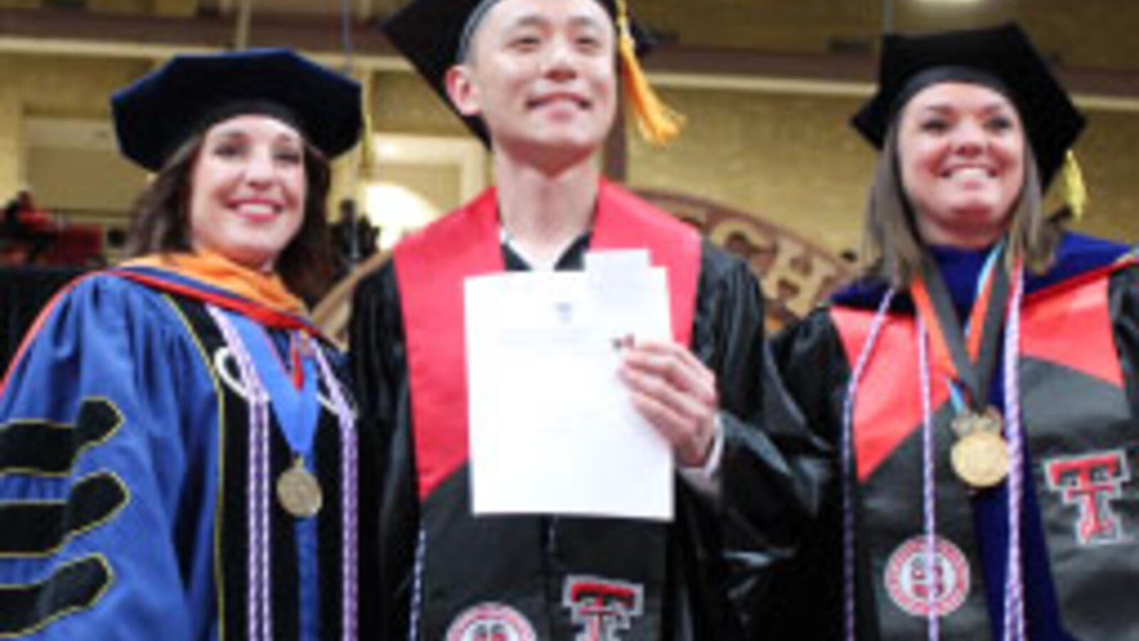 Male TTUHSC nursing student receives his degree and stands with two female faculty members at graduation.