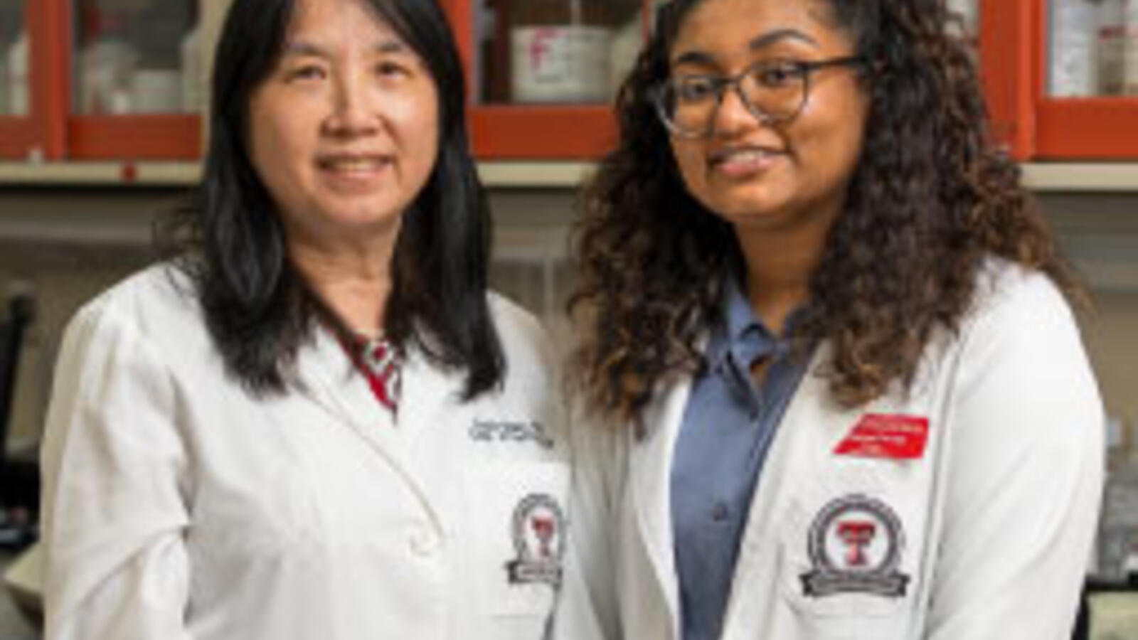 Two women stand together wearing white coats.