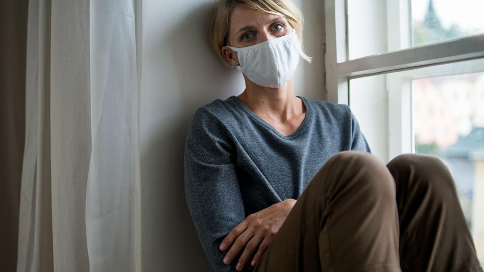 woman in COVID-19 mask sitting by a window