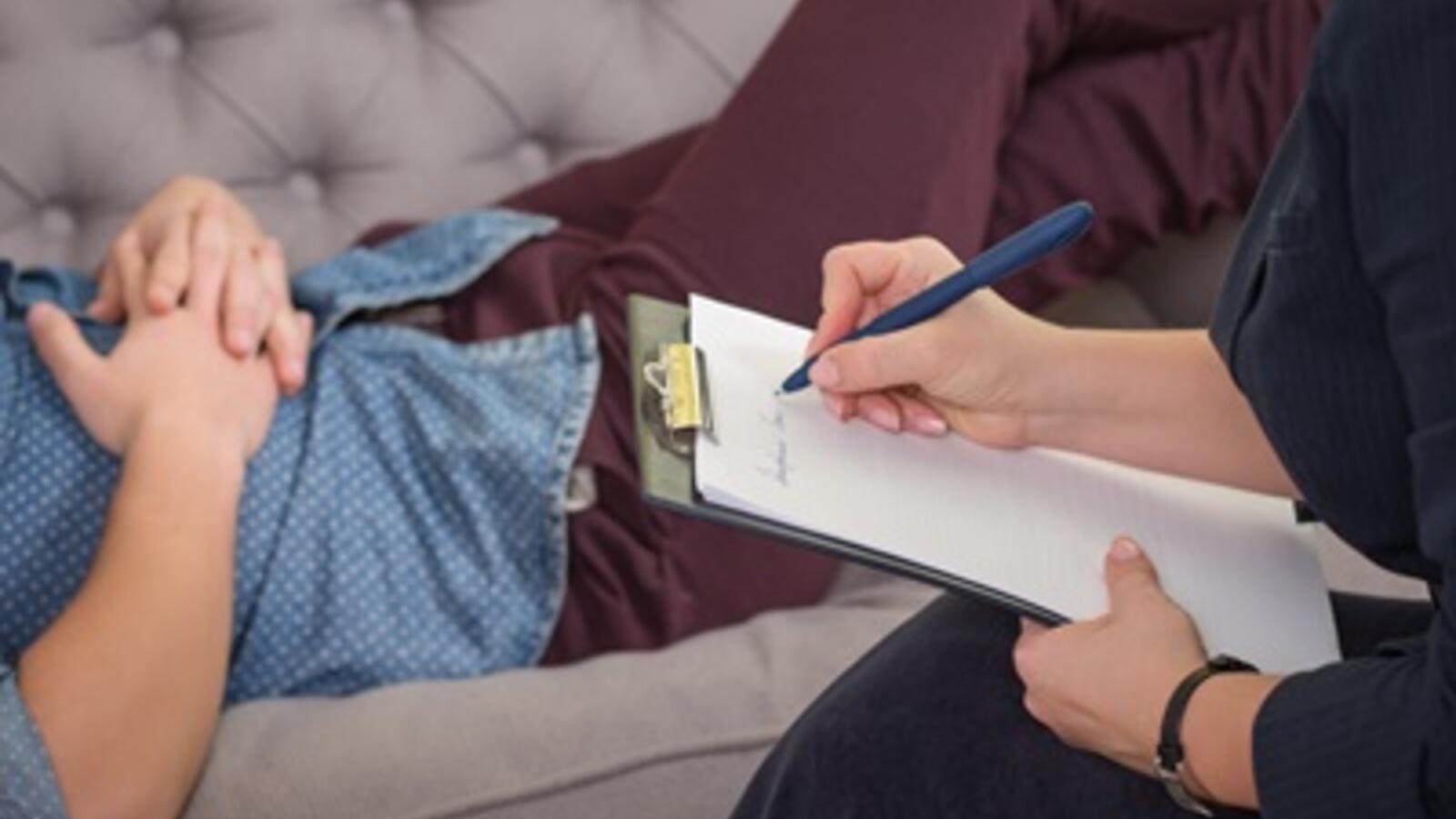 person lying on couch for therapy while a therapist takes notes
