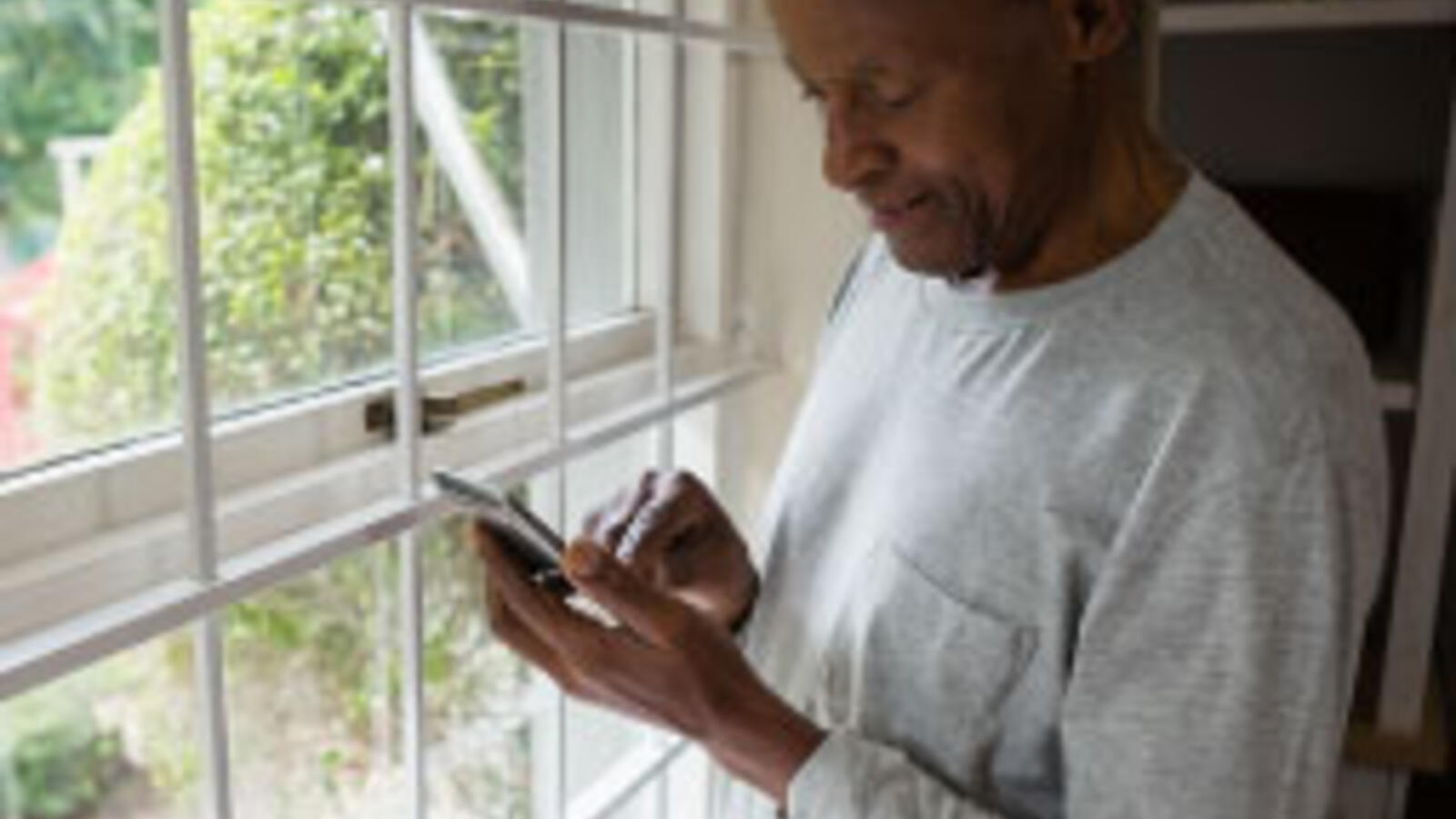 Elderly man on the phone standing at the window.