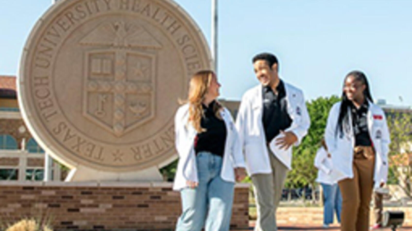 Several medical students walk outside in front of the TTUHSC university seal.