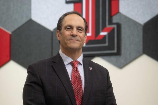 Portrait of the TTUHSC Provost standing in a conference room in front of a Texas Tech logo wall.