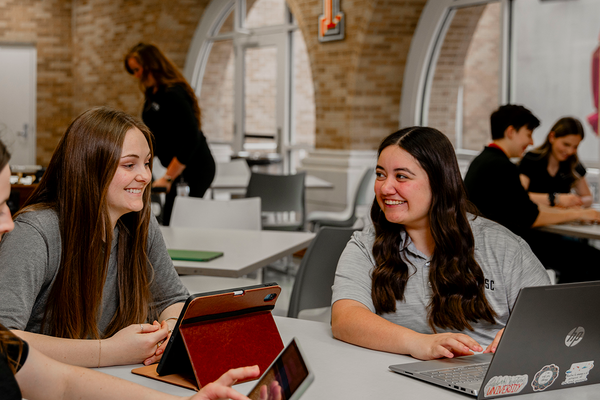 Two women sitting at a table with there laptops on the table.