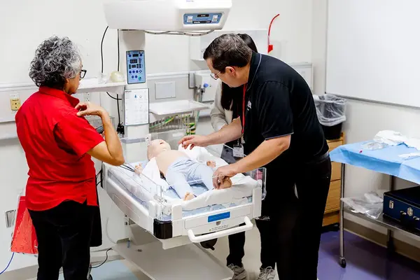 Instructor demonstrating newborn care on an infant simulator in a clinical training lab