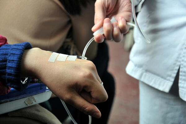 A close-up of a medical professional wearing blue gloves adjusting clear IV tubing on a patient's arm.