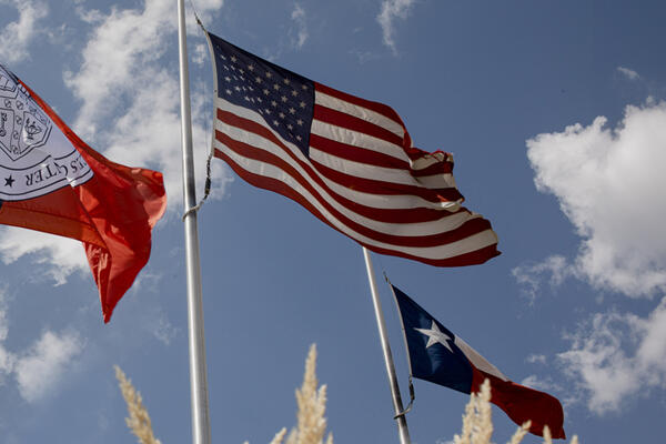 Texas Tech University Health Sciences Center, United States, and Texas flags flying against a bright blue sky with scattered white clouds.