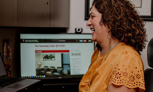 A team member participates in a virtual meeting at a desk, with the TTUHSC counseling services webpage displayed on a computer monitor.