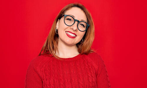 Person wearing glasses and a red sweater, posed against a bright red background.