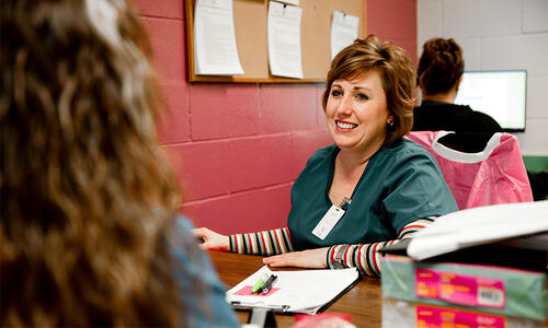 TTUHSC team member seated at a desk with paperwork, speaking with another person in a clinical office setting