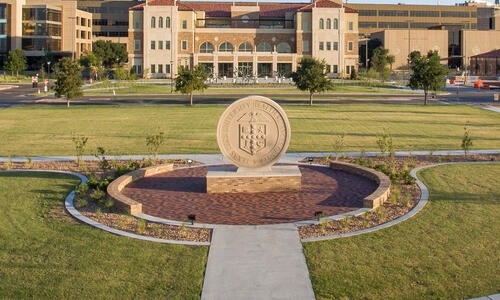 Aerial view of the TTUHSC University Center and campus grounds, featuring a large stone university seal surrounded by landscaped walkways and green lawns.