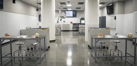 Medical gross anatomy laboratory with stainless steel examination tables and overhead light fixtures.