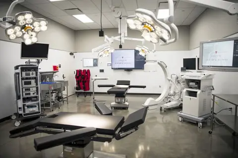 A modern surgical suite equipped with operating tables, overhead surgical lights, C-arm imaging equipment, and display monitors.