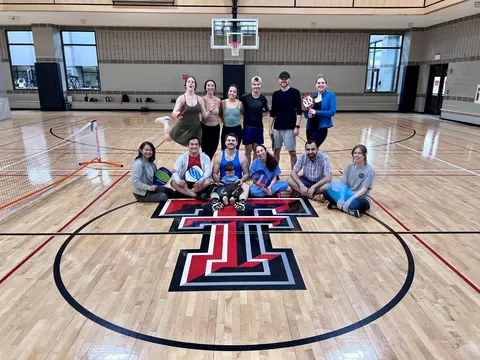 A group of surgery residents posing together on a basketball court with pickleball paddles, gathered around the center-court Texas Tech logo.