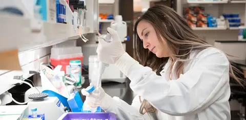 Researcher in a white lab coat using a pipette to prepare samples in a laboratory.