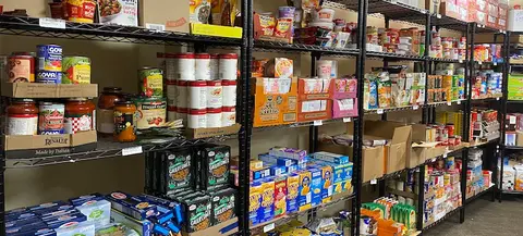 Shelves stocked with canned goods, pasta, cereal, snacks, and other nonperishable food items in a campus food pantry.