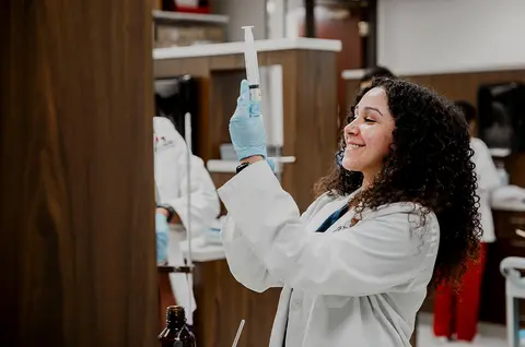 Pharmacy student wearing gloves examines a syringe in a laboratory.