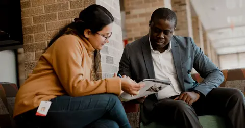 Two colleagues reviewing a brochure together in a campus seating area.