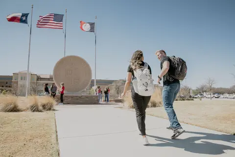 Students walking toward the TTUHSC seal and flags on campus.
