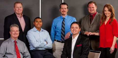 Seven alumni advisory board members pose together in professional attire in front of a dark backdrop.