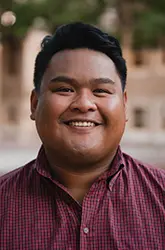 Headshot of Alvin Santos wearing a red-and-black patterned button-up shirt, smiling warmly at the camera.