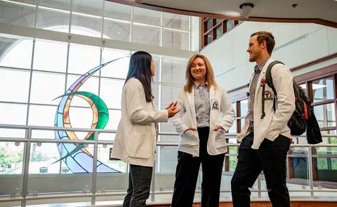 Three TTUHSC students in white coats talk inside the Amarillo campus.