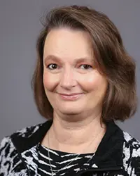 Headshot of Belinda Gallegos wearing a black-and-white patterned jacket, smiling against a gray background.