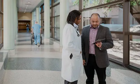 Two team members standing in a bright clinical corridor, looking down at a tablet