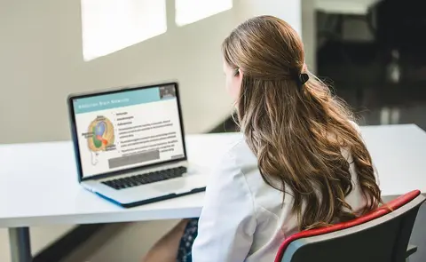 Person in a white coat viewing an online educational presentation on a laptop.