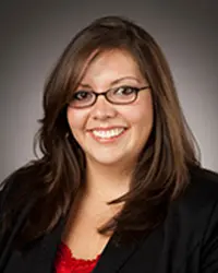 Headshot of Elisa Perez wearing glasses and a dark blazer over a red top, smiling warmly at the camera.