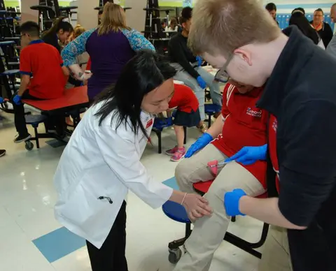 Students practice examining a knee during a hands-on healthcare activity.