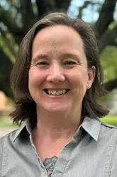 Headshot of Megan Hill wearing a gray collared shirt, smiling outdoors.