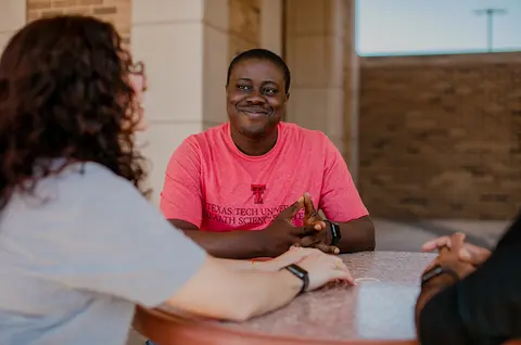 Three TTUHSC students sit together and talk around a table.