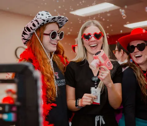 TTUHSC team members wearing playful hats and heart-shaped sunglasses while posing for a video.
