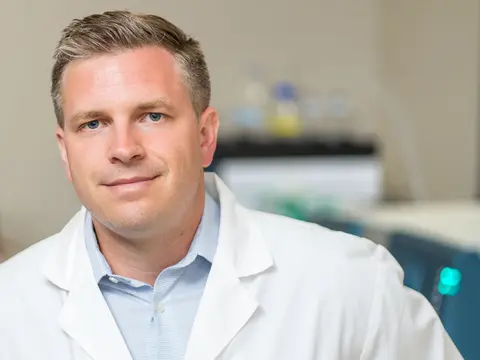 Aric Logsdon wears a white coat and sits in his lab.