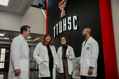 Group of students in white coats visiting on stairs inside academic building.