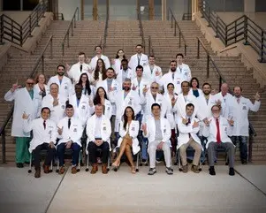 A group of medical professionals wearing white lab coats, poses together outdoors on a large set of outdoor stone steps.