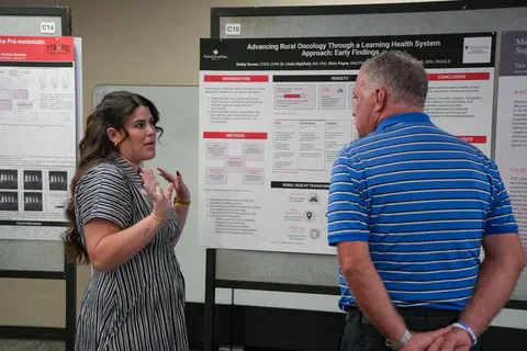 Student standing in front of poster presenting research on Rural Oncology through learning health system