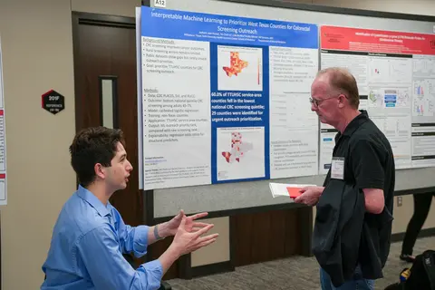 Student presenting research standing in front of their research poster on rural oncology and colorectal screening