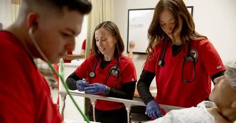 school of nursing students working with stethoscopes in red scrubs
