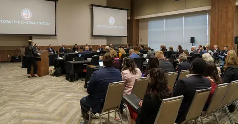 A large number of people sit at a meeting in a large room.