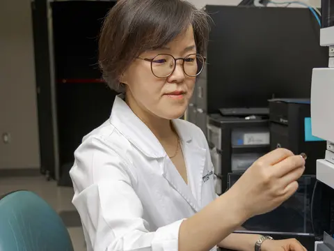 Female TTUHSC researcher wears a white coat and works in her lab.