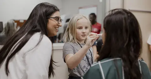 Elementary school student shining a light in the eye of a medical student for Docs for a Day
