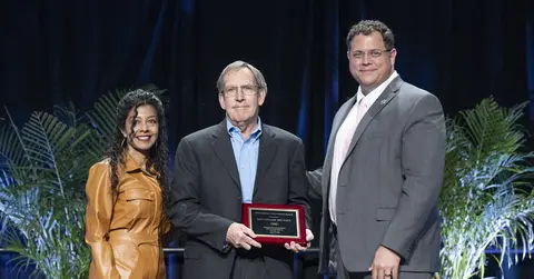 three people standing with awards on a stage