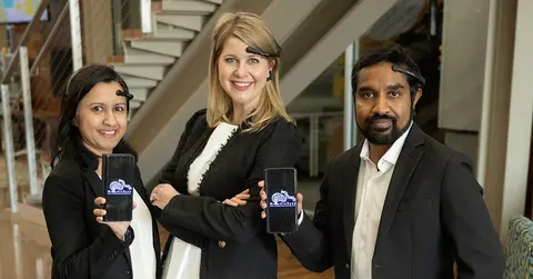 Three people posing, two of them showing iphones sporting a graphic on the screens