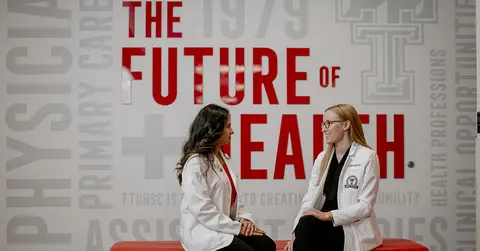 two women in lab coats talking on a bench